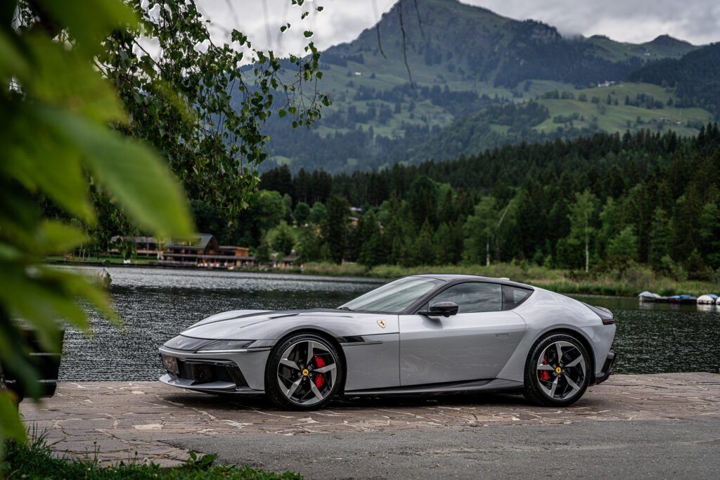 Grauer Sportwagen parkt am Seeufer vor Bergkulisse